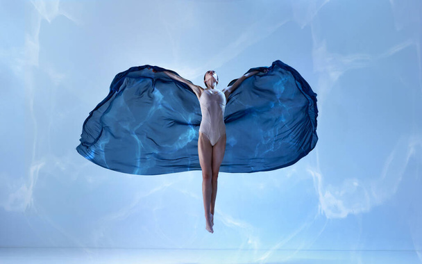 Motyl. Młoda balerina lecąca wdzięcznym ruchem z jedwabną tkaniną na niebieskim tle. Sztuka, ruch, działanie, elastyczność, koncepcja inspiracji. Piękno tańca współczesnego - Zdjęcie, obraz