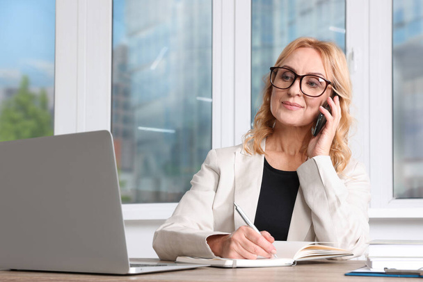 Lady boss talking on smartphone near laptop in office. Successful businesswoman - Photo, Image