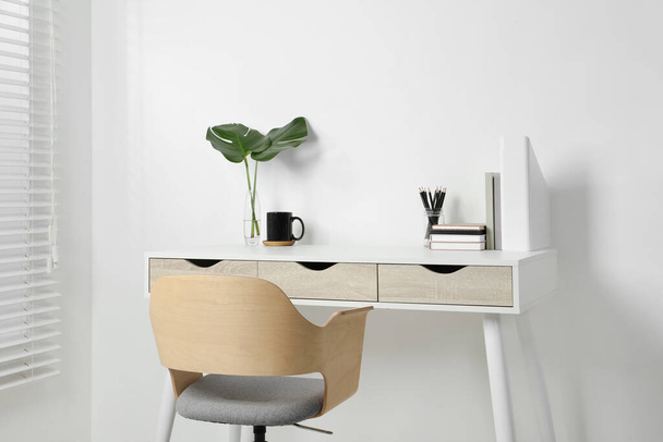 Удобное рабочее место с белым столом возле стены в помещении - Фото, изображение