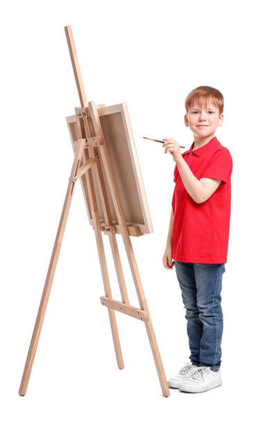 Little boy painting against white background. Using easel to hold canvas - Foto, Bild