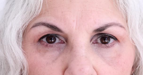Ηλικιωμένη γυναίκα με γκρίζα μαλλιά και καστανά μάτια φαίνεται τεταμένη σε κάμερα closeup αργή κίνηση. Ώριμη κυρία σοκαρισμένη από τρομακτικά γεγονότα. έκφραση συναισθημάτων - Πλάνα, βίντεο