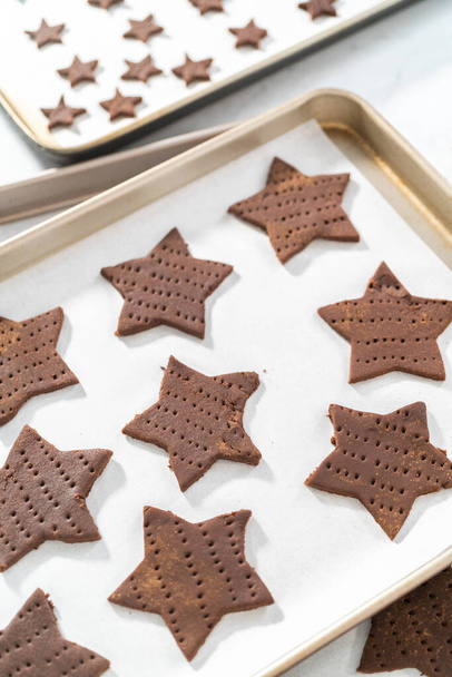 Cracker al cioccolato graham a forma di stella non cotti sulla teglia rivestita con carta da forno. - Foto, immagini
