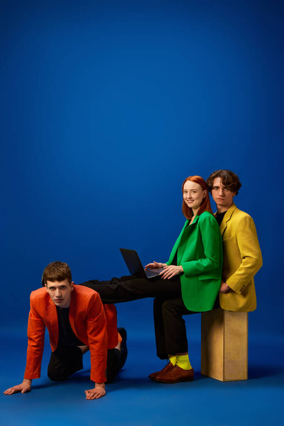 Sacrificing comfort for success. Group of young people wearing stylish clothes doing their job over blue background. Concept of fashion, models, style, business, online, teleworking, promotion - Photo, image