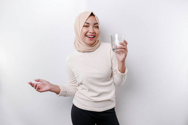 Joyful Asian Muslim woman wearing headscarf is drinking a glass of water, isolated on white background. - Foto, immagini