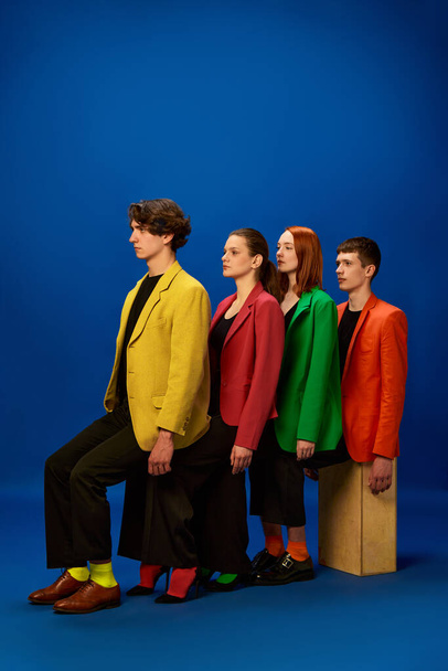 Support, aid, help. Men and women wearing colorful jackets sitting on each other knees over blue background. Concept of fashion, models, style, business, online, teleworking, promotion - Foto, imagen