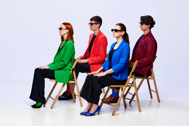 Διαδικασία μελέτης. Ομάδα νέων ανθρώπων, φοιτητής φορώντας πολύχρωμα κομψά μπουφάν κάθεται στην καρέκλα και κοιτάζοντας μακριά πάνω από το λευκό φόντο. Έννοια της εκπαίδευσης, της μόδας, των μοντέλων, το στυλ, τη ζωή των μαθητών - Φωτογραφία, εικόνα