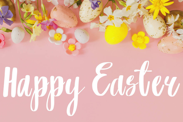 Happy Easter text sign on stylish eggs and blooming flowers on pink background flat lay. Modern Easter greeting card. Handwritten lettering - Foto, afbeelding