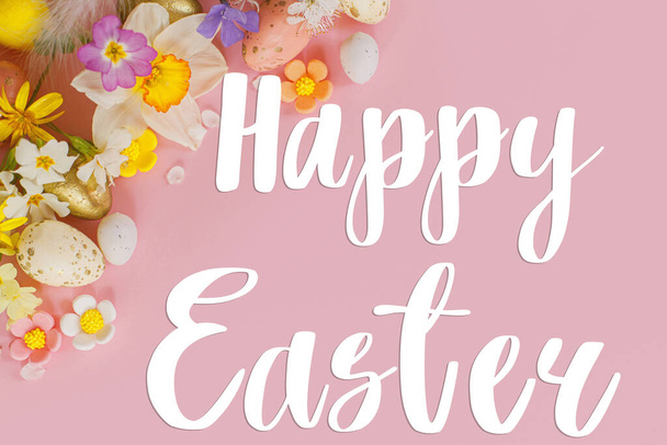 Gelukkige Pasen wenskaart. Happy Easter tekst op stijlvolle eieren en bloeiende lentebloemen op roze achtergrond plat leggen. Moderne wenskaart. Handgeschreven teken - Foto, afbeelding