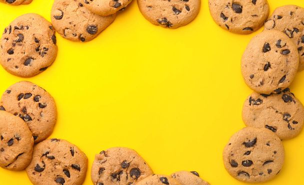 Frame made of many delicious chocolate chip cookies on yellow background, flat lay. Space for text - Foto, imagen