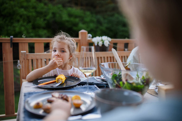 A family eating at barbecue party dinner on patio, little girl eating roasted corn and enjoying it. - Fotoğraf, Görsel