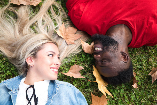 Feliz casal interracial deitado na relva. Casal olha um para o outro com felicidade. - Foto, Imagem