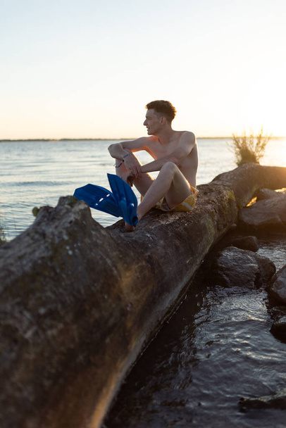 Young man sitting on tree stump in lake during sunset. - Fotó, kép
