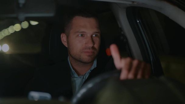 Close up of handsome young Caucasian businessman in suit driving car at night and smiling looking around. Man traveling in car from work. Taxi driver works in evening. Slow motion. Luxury style - Zdjęcie, obraz