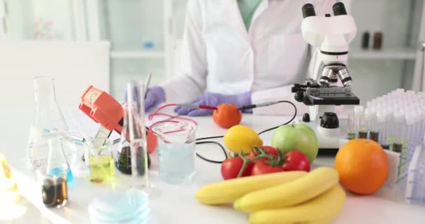 Cientista fêmea verifica o teor de nitratos em frutas e legumes frescos usando equipamentos de laboratório. Mulher escreve resultados de exame câmera lenta - Filmagem, Vídeo