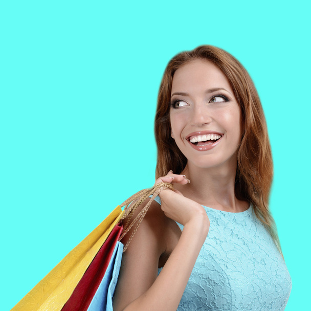 Beautiful young woman with shopping bags on turquoise background - Photo, Image