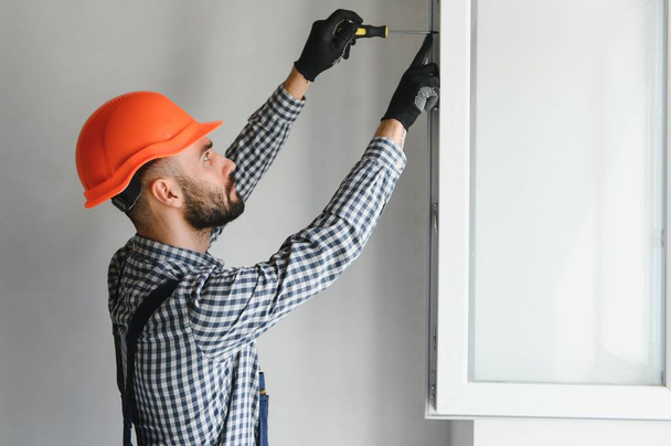 Workman in overalls installing or adjusting plastic windows in the living room at home. - Foto, imagen