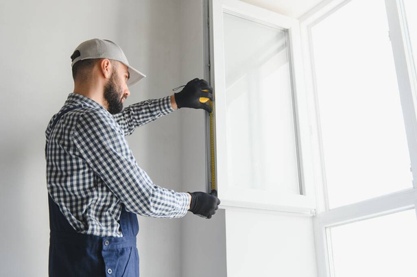 Worker installing plastic window indoors. - Фото, изображение