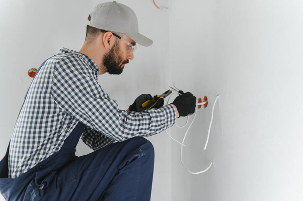 Professional electrician working on a home electrical system, he is installing a wall socket. - Фото, зображення
