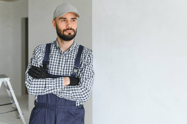 Portrait of handsome mechanic with stubble in blue overall, shirt having his arms crossed, looking at camera. - 写真・画像