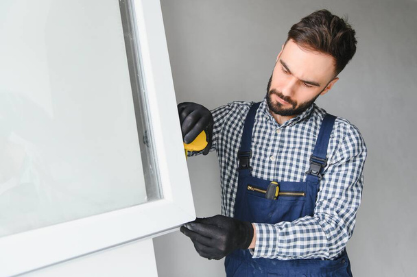 Workman in overalls installing or adjusting plastic windows in the living room at home. - Foto, Imagem