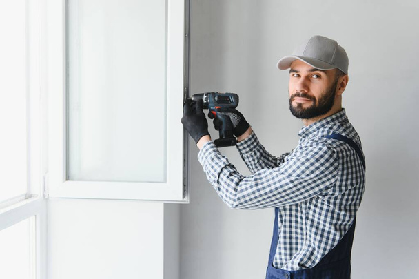 Workman in overalls installing or adjusting plastic windows in the living room at home. - Foto, Bild