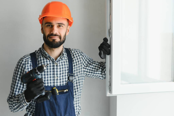 Workman in overalls installing or adjusting plastic windows in the living room at home. - 写真・画像