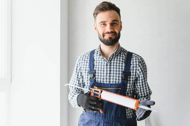 Contractor hand holding glue gun with silicone to repair tile and window. Installation or renovation interior concept - 写真・画像