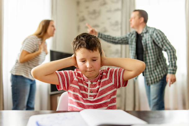 Uma criança triste cobre os ouvidos com as mãos durante uma discussão entre os pais. Conflitos familiares ou impacto do divórcio no desenvolvimento infantil - Foto, Imagem