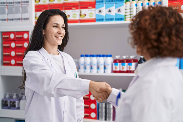 Дві жінки-фармацевти посміхаються впевнено потиснути руки в аптеці
 - Фото, зображення