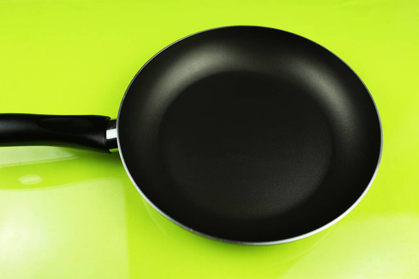 Eine leere Pfanne auf gelb-grünem Hintergrund. Nahaufnahme schwarzer Küchengeräte. Vorbereitung zum Braten. Vorbereitung des Frühstücks. Bratpfanne Schwarze Metallutensilien. - Foto, Bild