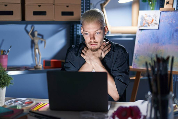 Jonge blanke man die 's nachts laptop gebruikt in de kunststudio schreeuwt en stikt omdat hij gewurgd is. gezondheidsproblemen. verstikking en zelfmoordconcept.  - Foto, afbeelding