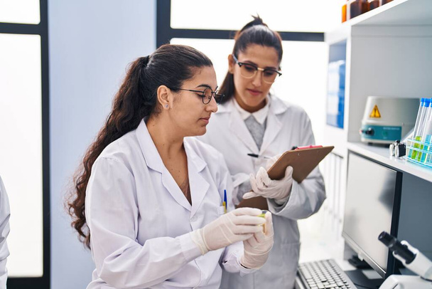 Τρεις γυναίκες επιστήμονες που κρατούν δείγμα γράφουν στον κατάλογο ελέγχου στο εργαστήριο - Φωτογραφία, εικόνα
