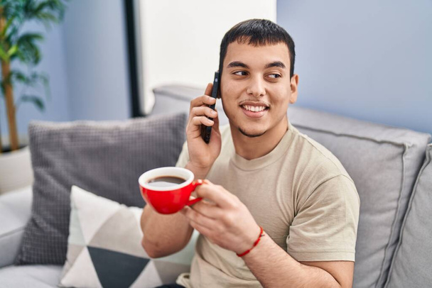 Young man drinking coffee and talking on the smartphone at home - Fotoğraf, Görsel