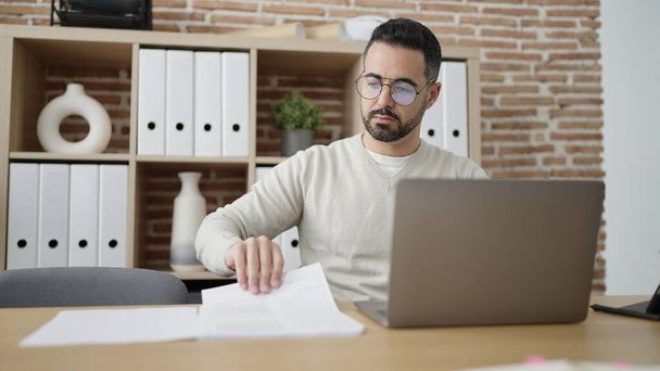 Молодой латиноамериканец-бизнесмен пользуется документом для чтения ноутбуков в офисе - Фото, изображение