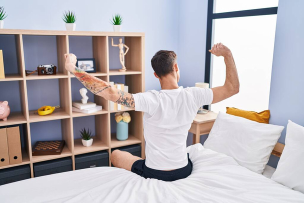 Молодой человек просыпается с протянутыми руками на заднем плане в спальне - Фото, изображение
