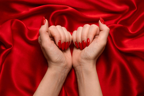 Beautiful red manicure on woman hands on a luxury red silk backround.  - Фото, зображення