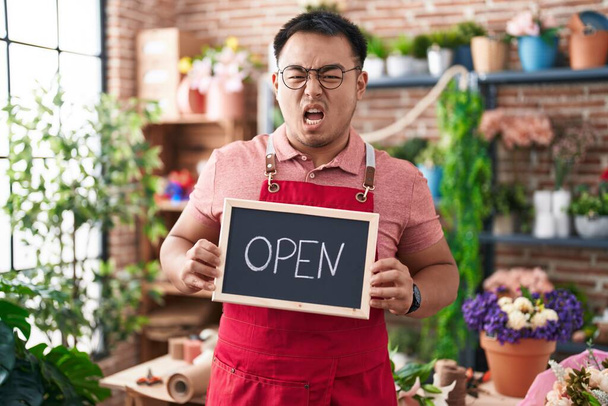 Chinese young man working at florist holding open sign angry and mad screaming frustrated and furious, shouting with anger. rage and aggressive concept.  - Photo, Image