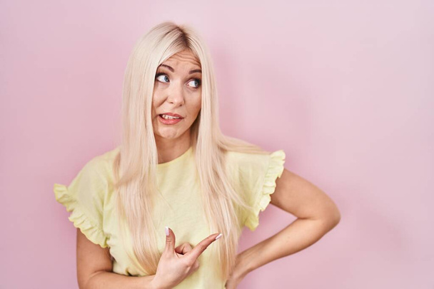 Caucasian woman standing over pink background pointing aside worried and nervous with forefinger, concerned and surprised expression  - Foto, Bild