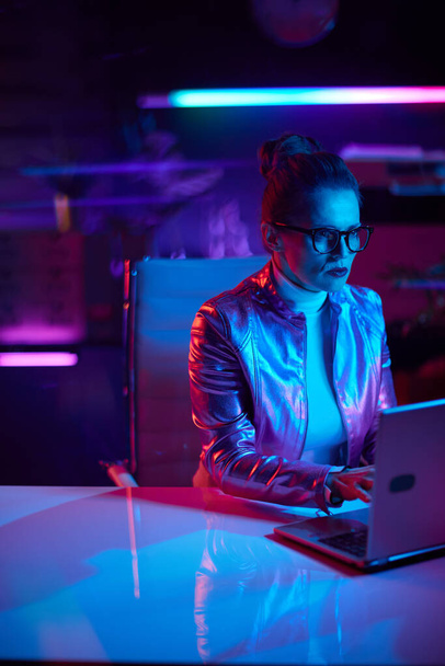 Neon metaverse futuristic concept. pensive trendy woman in glasses with laptop in modern office. - Valokuva, kuva