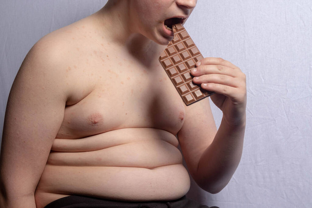 Un adolescent caucasien en surpoids qui mange une barre de chocolat au lait - Photo, image