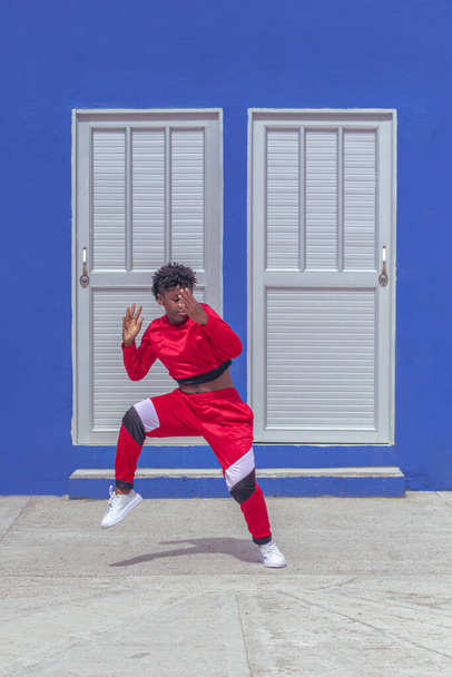 Jover mujer afro realizar baile estilo urbano en parque local con pared azul y puertas de fondo - Foto, Imagen