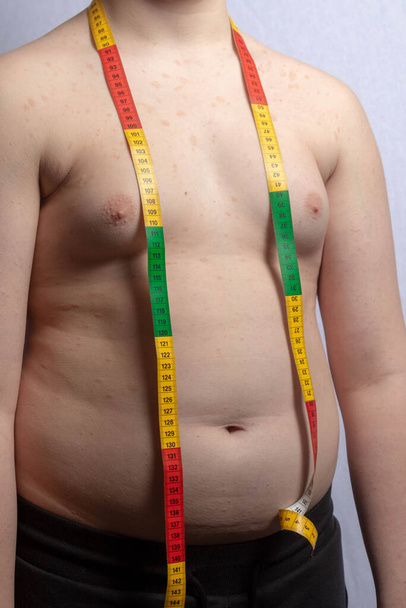 An overweight caucasian teenage boy with a tape measure round his neck - Foto, imagen