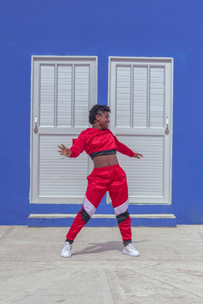 Jover mujer afro realizar baile estilo urbano en parque local con pared azul y puertas de fondo - Foto, Imagen