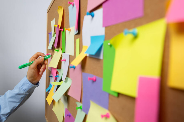 A business woman's hand writes on sticky notes attached to a cortical bulletin board. - Photo, image