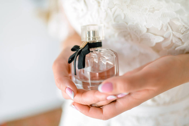 Bottle perfume in bride hands. Female hands holding a bottle of elite perfume. Mock-up with blank transparent bottle. High quality photo - 写真・画像