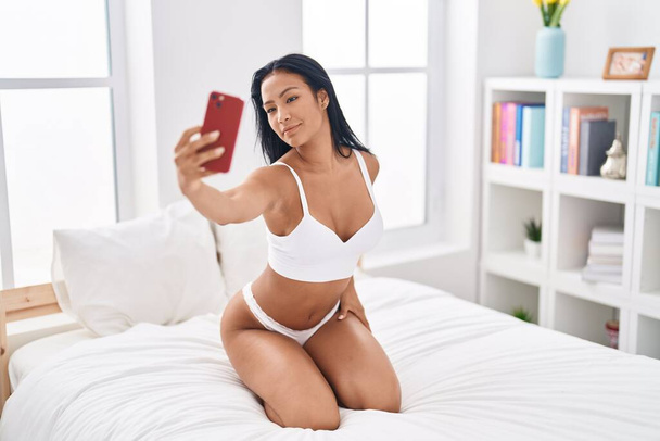 Young beautiful latin woman wearing lingerie make selfie by smartphone at bedroom - Photo, Image