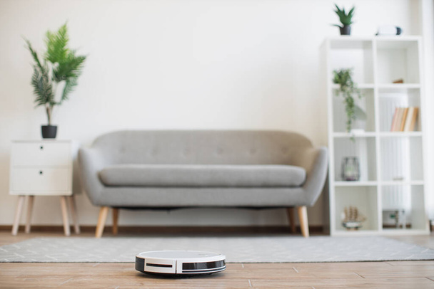Automatic robot vacuum moving from soft carpet to hardwood floor while removing dust in living room. Smart home device conducting daily vacuuming and saving residents from seasonal allergies. - Photo, image