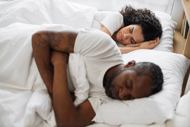 Young multicultural family of two in casual clothing having deep dream before awaking early in morning. Romantic partners sharing relationship closeness by sleeping on same sides under one blanket. - Fotó, kép