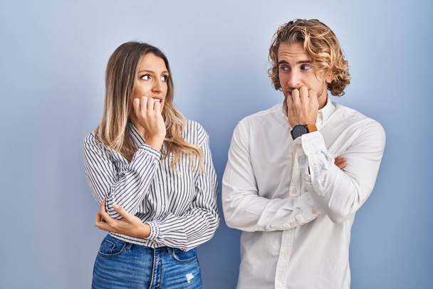 Young couple standing over blue background looking stressed and nervous with hands on mouth biting nails. anxiety problem.  - Foto, Bild