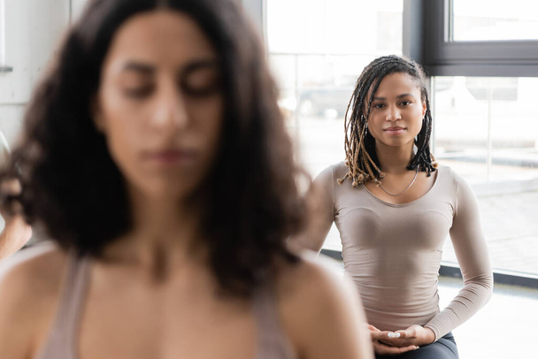 Young african american woman looking at camera near blurred people in yoga class  - Фото, изображение